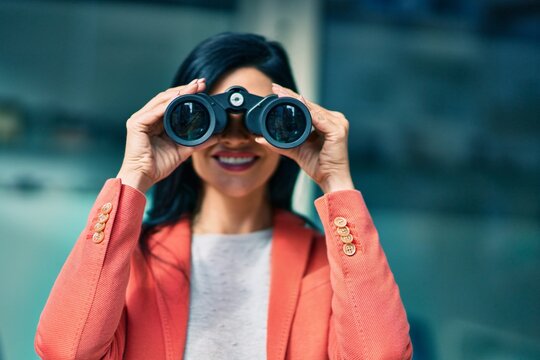 Young beautiful businesswoman smiling happy looking for new opportunities using binoculars at the city.