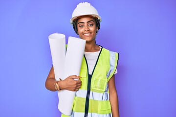 Young african american woman with braids wearing safety helmet holding blueprints looking positive and happy standing and smiling with a confident smile showing teeth