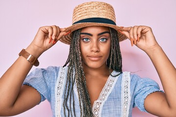 Young african american woman with braids wearing summer hat relaxed with serious expression on...