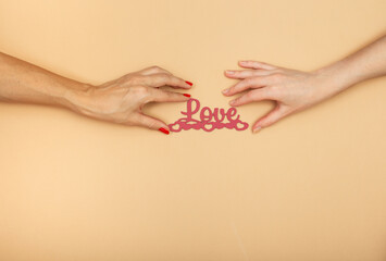 LGBT concept. Women hands holding red text Love on beige background. Hands of homosexual couple on set sail champagne color. Same sex love. Lesbi Valentines card with copy space