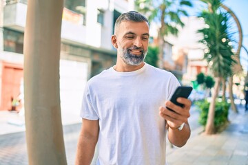 Middle age grey-haired man smiling happy using smartphone at the city