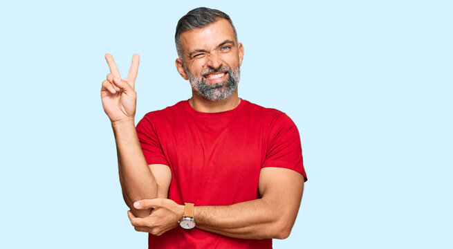 Middle age handsome man wearing casual clothes smiling with happy face winking at the camera doing victory sign. number two.