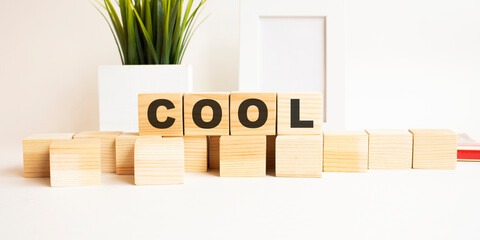 Wooden cubes with letters on a white table. The word is COOL. White background.