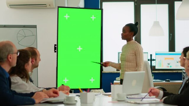 African businesswoman analysing annual financial reports standing in conference room pointing at green screen monitor. Leader explainig project strategy using greenscreen pc with chroma key display