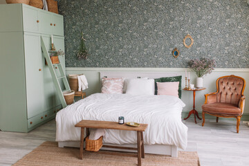 Bedroom in green Scandinavian style Wardrobe with baskets for things Bed with pink and green pillows Table with candles and dried flowers Vintage brown armchair