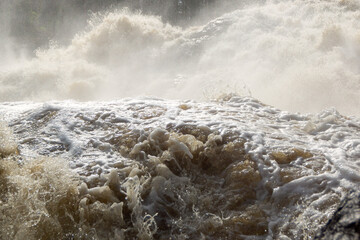 Water of river breaks on sharp rocks in waterfall with splashes and foam