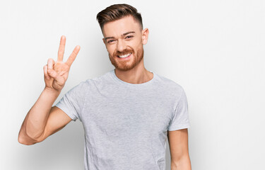 Fototapeta premium Young redhead man wearing casual grey t shirt showing and pointing up with fingers number two while smiling confident and happy.