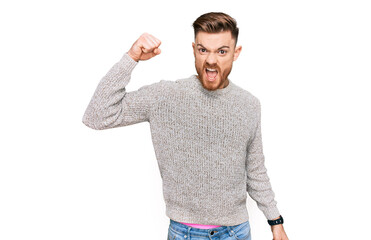 Young redhead man wearing casual winter sweater angry and mad raising fist frustrated and furious...