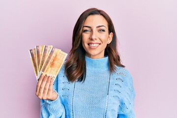 Young brunette woman holding 500 norwegian krone banknotes looking positive and happy standing and...