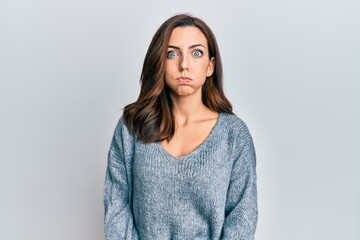 Young brunette woman wearing casual winter sweater puffing cheeks with funny face. mouth inflated with air, crazy expression. - obrazy, fototapety, plakaty