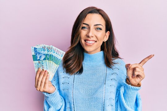 Young brunette woman holding hong kong 20 dollars banknotes smiling happy pointing with hand and finger to the side