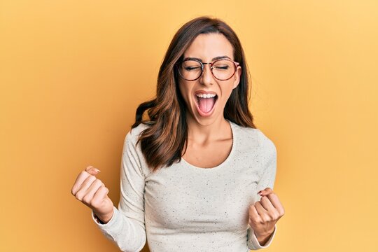 Young brunette woman wearing casual clothes and glasses celebrating surprised and amazed for success with arms raised and eyes closed