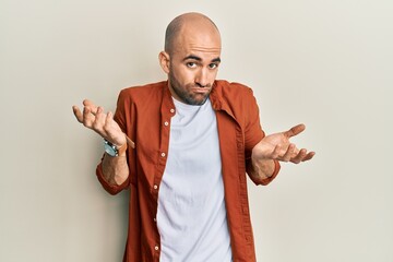 Young hispanic man wearing casual clothes clueless and confused with open arms, no idea and...