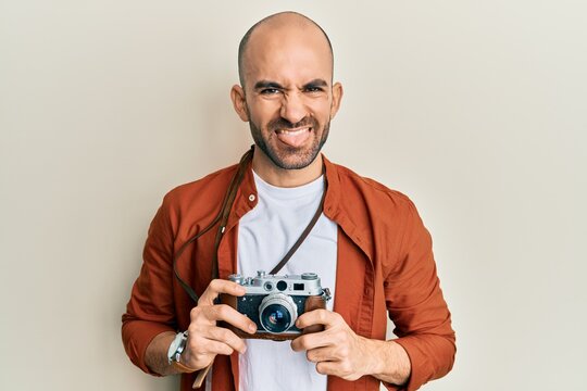 Young hispanic man holding vintage camera sticking tongue out happy with funny expression.