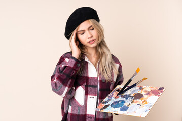 Teenager artist girl holding a palette isolated on blue background with headache
