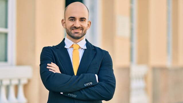 Young hispanic bald businessman with arms crossed smiling happy at the city.