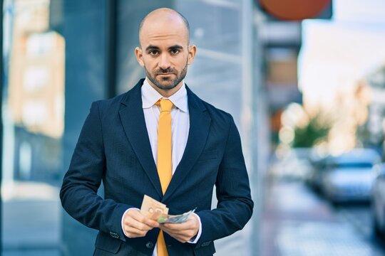 Young hispanic bald businessman with serious expression counting canadian dollars banknotes at the city.