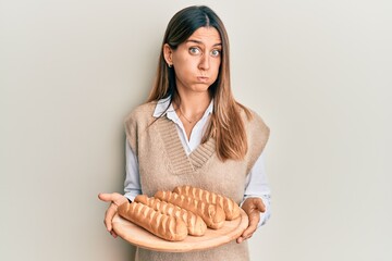 Brunette young woman holding homemade bread puffing cheeks with funny face. mouth inflated with...