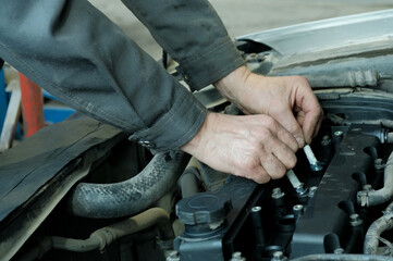 Replacement of spark plugs in the car engine. Close-up of the hands of an auto mechanic installing...