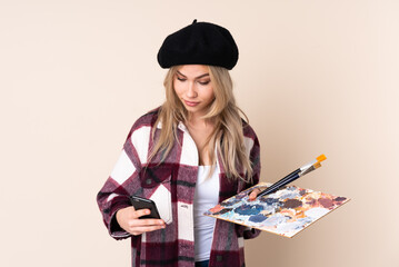 Teenager artist girl holding a palette isolated on blue background holding coffee to take away and...