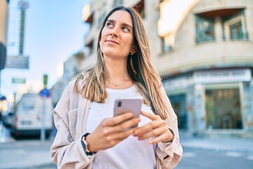 Fototapeta premium Young caucasian woman smiling happy using smartphone at the city.