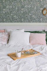 Spring interior in the bedroom, a tray with tea on the bed with green pillows and wallpaper Scandinavian style