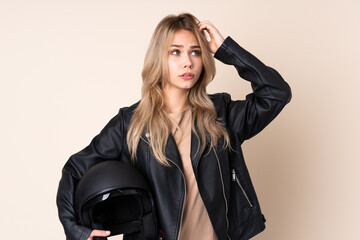 Russian girl with a motorcycle helmet isolated on beige background having doubts while scratching head