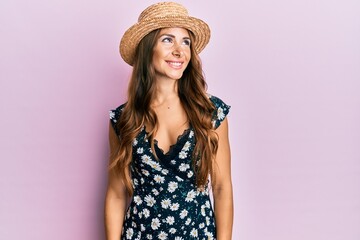 Young brunette woman wearing summer hat looking away to side with smile on face, natural expression. laughing confident.