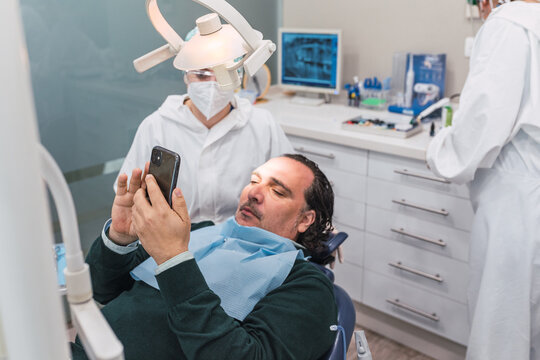 Patient using smartphone in dental office. Two female doctors preparing the procedure. concept of dental health and hygiene.