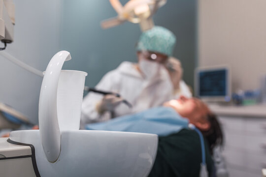 Glass of water in the dental office. Female doctor attending to a male patient. Focus on the white plastic cup.