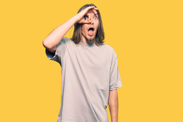 Handsome caucasian man with long hair wearing casual clothes doing ok gesture shocked with surprised face, eye looking through fingers. unbelieving expression.