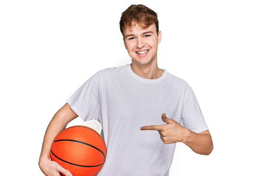 Young caucasian man holding basketball ball smiling happy pointing with hand and finger