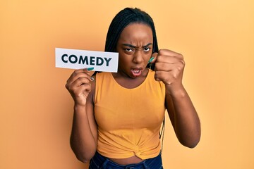 Young african american woman holding comedy word paper annoyed and frustrated shouting with anger, yelling crazy with anger and hand raised