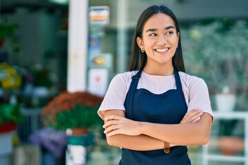 Young latin shopkeeper girl with arms crossed smiling happy standing at the florist