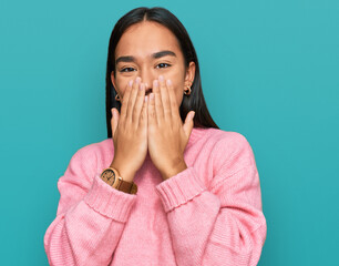 Young asian woman wearing casual winter sweater laughing and embarrassed giggle covering mouth with...