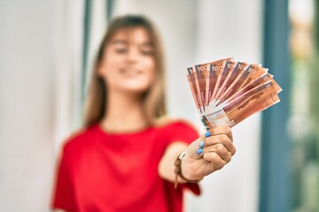 Caucasian teenager girl smiling happy holding norwegian krone at the city.