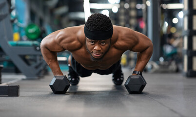 Fototapeta na wymiar Confident black guy sportsman pushing up with dumbbells