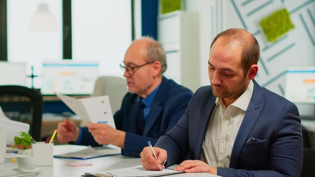 Businessman reading paper document, discussing contract with confident partner, signing investment papers. Executive director meeting shareholders in start up office, making satisfactorily agreement.