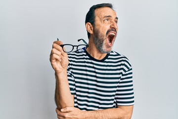 Middle age hispanic man wearing casual clothes and holding glasses angry and mad screaming...