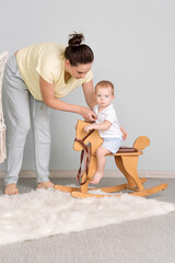 Tender Mom and Son. Child Sitting On Ride On Toy In Playroom. Toddler Baby Boy Riding Swinging On Rocking Chair Toy Horse.