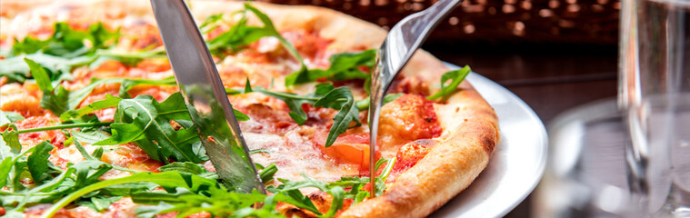 Banner of appetizing pizza in a cafe. The visitor cuts the pizza with a knife and fork at the table. Horizontal photo banner for website header design