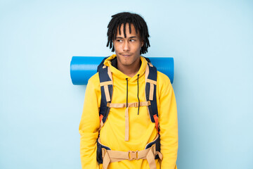 Young mountaineer african american man with a big backpack isolated on a blue background standing...