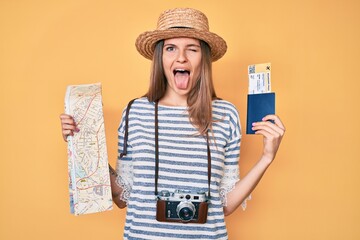 Beautiful caucasian tourist woman holding city map and passport sticking tongue out happy with funny expression.