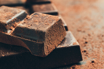 Chocolate bar and chopped chocolate cubes on dark background, close-up view