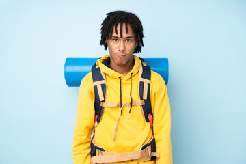 Young mountaineer african american man with a big backpack isolated on a blue background sad