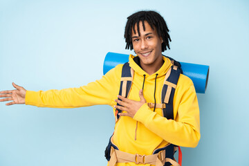 Young mountaineer african american man with a big backpack isolated on a blue background extending...