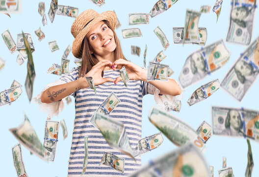 Beautiful caucasian woman wearing summer hat smiling in love doing heart symbol shape with hands. romantic concept.