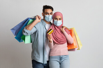 Happy muslim couple wearing masks holding credit card and paper shopping bags