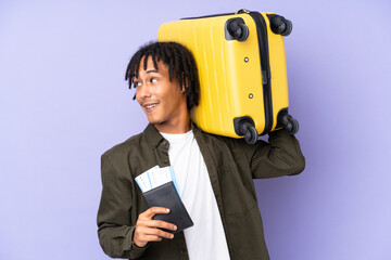 Young african american man isolated on purple background in vacation with suitcase and passport