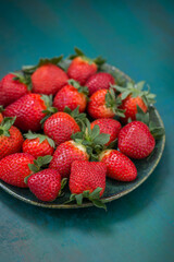 Ripe strawberries in a plate close-up on a blue-green background